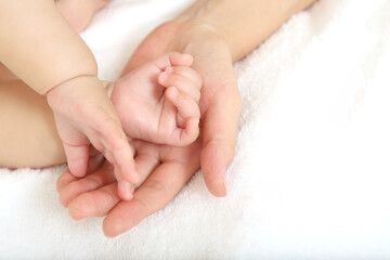 Baby little hand on mom's hand against white sheets background