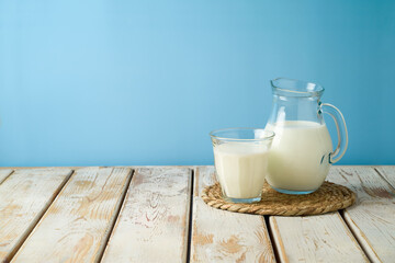 Milk jug and milk glass on wooden table over blue background. Kitchen mock up for design