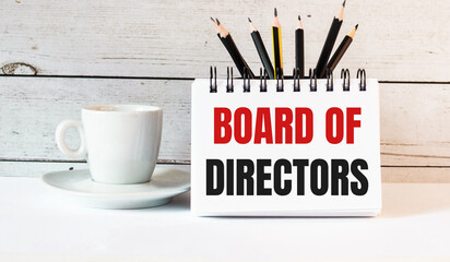 The words BOARD OF DIRECTORS is written in a white notepad near a white cup of coffee on a light...