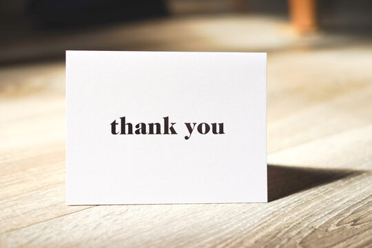White thank you card standing on wooden table. Modern minimalist composition. Special thank you note.