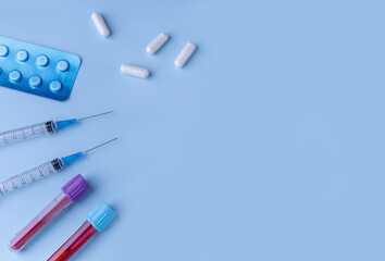 test tubes with blood tests, tablets, syringes with medication and capsules on a blue background....