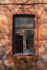 Window with broken glass and iron bars in a brick wall of an abandoned house