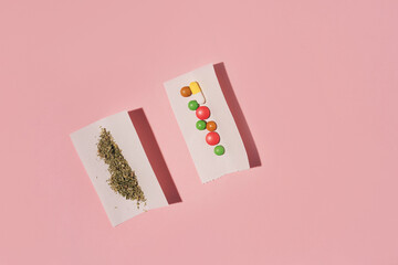 Two paper rolls with dry Marijuana and pills, flat lay on pink background