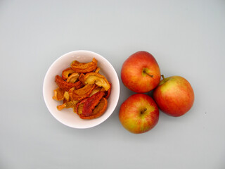 Cut into pieces dried apples in a white bowl and fresh juicy apples next to it.