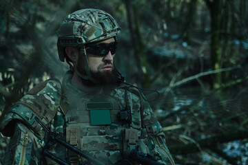 Portrait of airsoft player in professional equipment with machine gun in the forest. Soldier with...