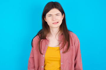 young beautiful Caucasian woman wearing pink jacket over blue wall being nervous and scared biting lips looking camera with impatient expression, pensive.