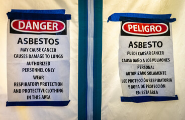 Bilingual signs in English and Spanish warns of the risk of lung cancer (and mesothelioma) from exposure to asbestos during remodeling of an old kitchen.   