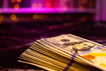 Big wad money hundred dollar bills on pink background in macro with bokeh. Theme of cash settlement in brothel or casino. USD with copy space place in purple lighting and image of President Franklin