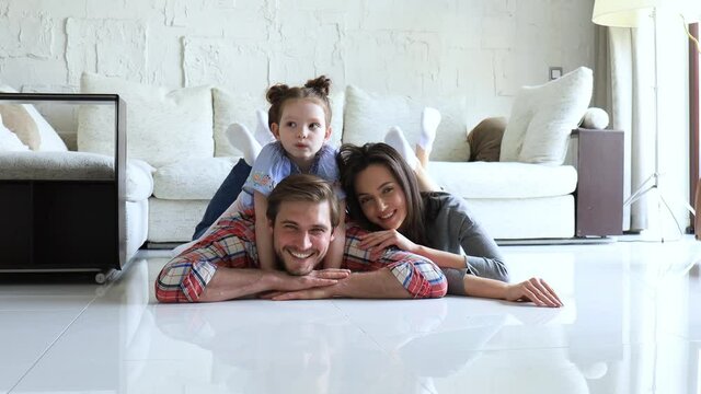 Young caucasian family with small daughter pose relax on floor in living room, smiling little girl kid hug embrace parents, show love and gratitude, rest at home together.