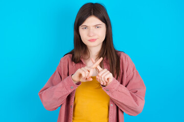 young beautiful Caucasian woman wearing pink jacket over blue wall has rejection angry expression...