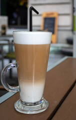 Coffee with milk in a glass with a straw on a brown coffee shop table, cafe latte, outdoors