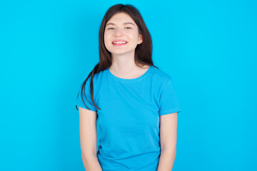 young beautiful Caucasian woman wearing blue T-shirt over blue wall with nice beaming smile pleased expression. Positive emotions concept