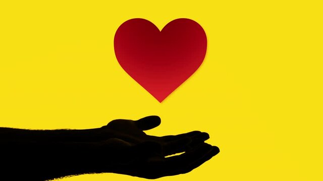 Silhouetted profile shot: two male hands appearing, united, ready to collect a digitally drawn heart (red shape, yellow background).
