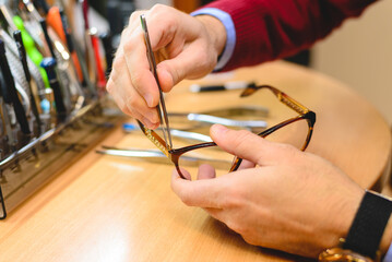 Close up of male optometrist hands repairing pair of eyeglasses