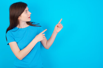 young beautiful Caucasian woman wearing blue T-shirt over blue wall smile excited directing fingers look empty space