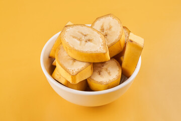 White cup with sliced bananas on a yellow background. Tropical fruits, healthy food, vitamins