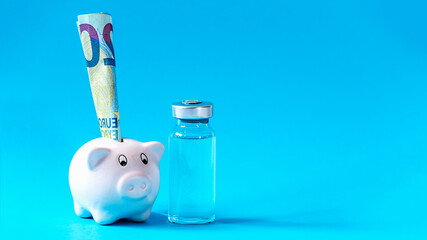 Covid 19 vaccina cost concept. Glass vial and piggy bank stands on blue background.