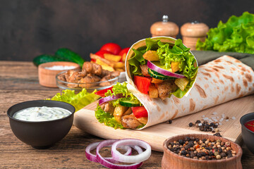 Juicy shawarma with fresh vegetables, meat and French fries on a brown wooden background.