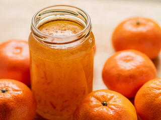 orange fruits surrounding a jar of orange marmalade no label on the jar