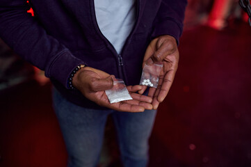 Drug addict man holds package of pills and powder
