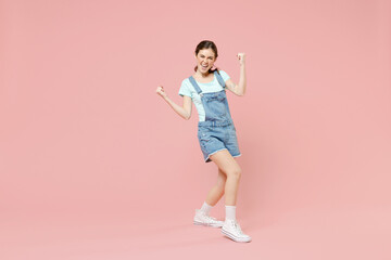 Full length young overjoyed successful happy caucasian woman in denim clothes blue t-shirt do winner gesture clench fist isolated on pastel pink background studio portrait People lifestyle concept