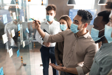 Businesspeople having meeting using sticky post-it notes on glass wall