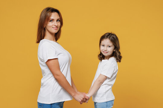 Happy woman in basic white t-shirt have fun with cute child baby girl 5-6 years old hold hands. Mommy little kid daughter isolated on yellow color background studio. Mother's Day love family concept.
