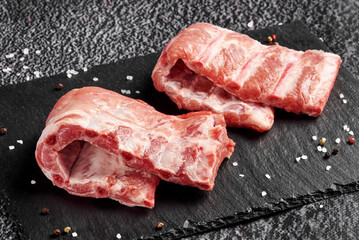 raw beef ribs on black stone background with salt and pepper