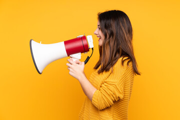 Young caucasian woman isolated on yellow background shouting through a megaphone