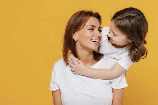 Happy woman in white t-shirt have fun with cute child baby girl 5-6 years old stand behind Mommy little kid daughter isolated on yellow orange color background studio Mother's Day love family concept