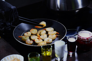 The cook is frying shrimps in a frying pan. Dark background. An unrecognizable person.