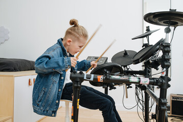 Energetic little boy playing electronic drums at home with passion