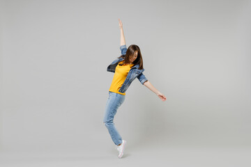 Full length side view young caucasian woman in casual denim jacket yellow t-shirt looking aside leaning back stand on toes dancing isolated on grey background studio portrait People lifestyle concept. - obrazy, fototapety, plakaty