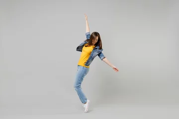 Foto op Plexiglas Full length side view young caucasian woman in casual denim jacket yellow t-shirt looking aside leaning back stand on toes dancing isolated on grey background studio portrait People lifestyle concept. © ViDi Studio