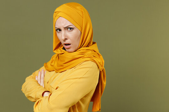 Side view indignant confused young arabian asian muslim woman in abaya hijab yellow clothes hold hand cross folded isolated on olive green background People uae middle eastern islam religious concept