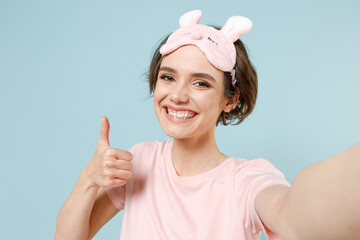 Fototapeta na wymiar Close up young woman in pajamas jam sleep eye mask rest relaxing at home do selfie shot mobile phone show thumb up isolated on pastel blue background studio portrait. Good mood night bedtime concept.