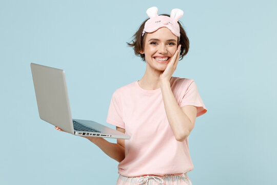 Smiling Fun Excited Surprised Young Woman In Pajamas Jam Sleep Eye Mask Rest Relax At Home Hold Laptop Pc Computer Hold Face Isolated On Pastel Blue Background Studio. Good Mood Night Bedtime Concept.