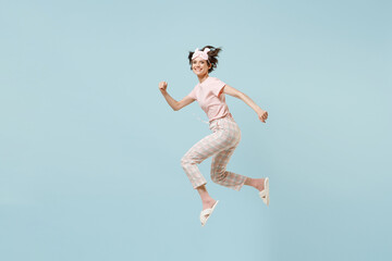 Fototapeta na wymiar Full length side view sporty young woman in pajamas jam sleep eye mask rest relax at home jump high running fast isolated on pastel blue background studio portrait. Good mood night bedtime concept