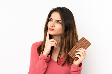 Young caucasian woman isolated on pink background taking a chocolate tablet and having doubts