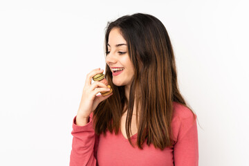 Young caucasian woman isolated on pink background holding colorful French macarons and eating it