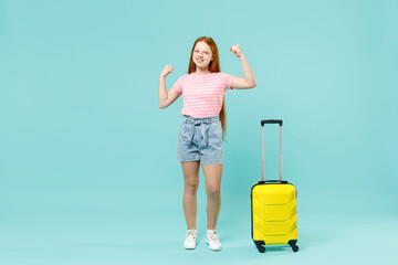 Full length traveler tourist kid girl 12-13 years old in pink t-shirt hold suitcase show muscles bicepse isolated on pastel blue background. Passenger travel abroad weekend Air flight journey concept.