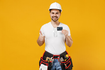 Young employee handyman man in protective helmet hardhat hold credit bank card show thumb up...