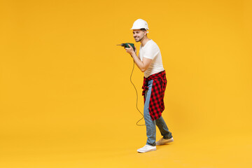 Full length young employee handyman man in protective helmet hardhat glasses hold electric drill isolated on yellow background Instruments accessories renovation apartment room Repair home concept