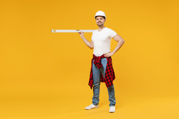 Full length young employee handyman man in protective helmet hold build bubble spirit level stand...