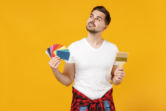 Young Fun Employee Handyman Man In T-shirt Hold Color Palette Paint Brush Look Overhead Isolated On Yellow Background Studio. Instruments Accessories For Renovation Apartment Room Repair Home Concept.