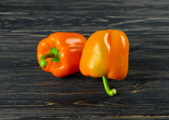 Two orange bell peppers close-up on a black wooden background.