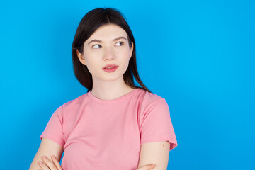 young beautiful Caucasian woman wearing pink T-shirt over blue wall looking aside into empty space thoughtful