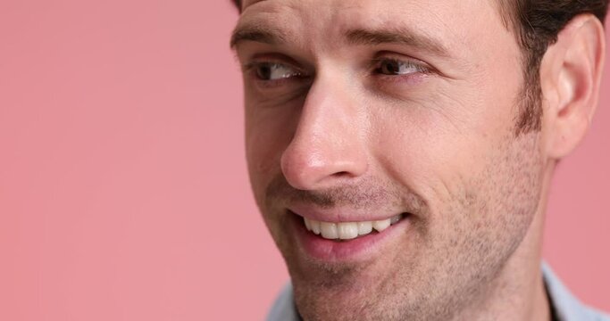 face close up of attractive unshaved man smiling, looking to side and nodding on pink background in studio