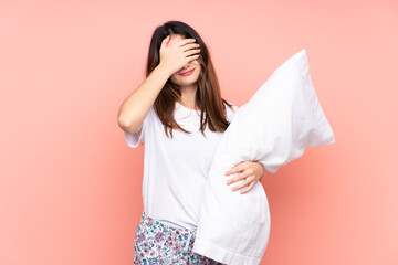 Young woman in pajamas isolated on pink background covering eyes by hands