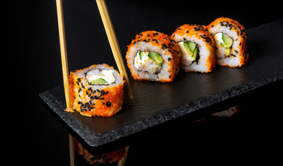 Traditional sushi and chopsticks. Philadelphia with salmon, avocado and cheese. Japanese cuisine on black background